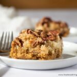 A slice of gluten-free pumpkin dump cake with pecans on a small white plate with a fork, and another slice in the background.