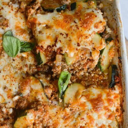 Close up of ground beef zucchini casserole covered with browned cheese, with a slice being lifted by a spoon.