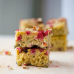Pieces of cranberry coffee cake, natural color with bright cranberries. 2 pieces are visible in the front and more are blurred in the background.