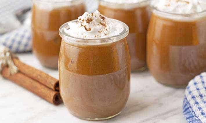 Sweet potato pudding in a glass, topped with whipped cream and cinnamon. Cinnamon sticks and more glasses of pudding in the background.