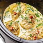 Crock pot bowl filled with chicken breasts in a creamy tuscan sauce.