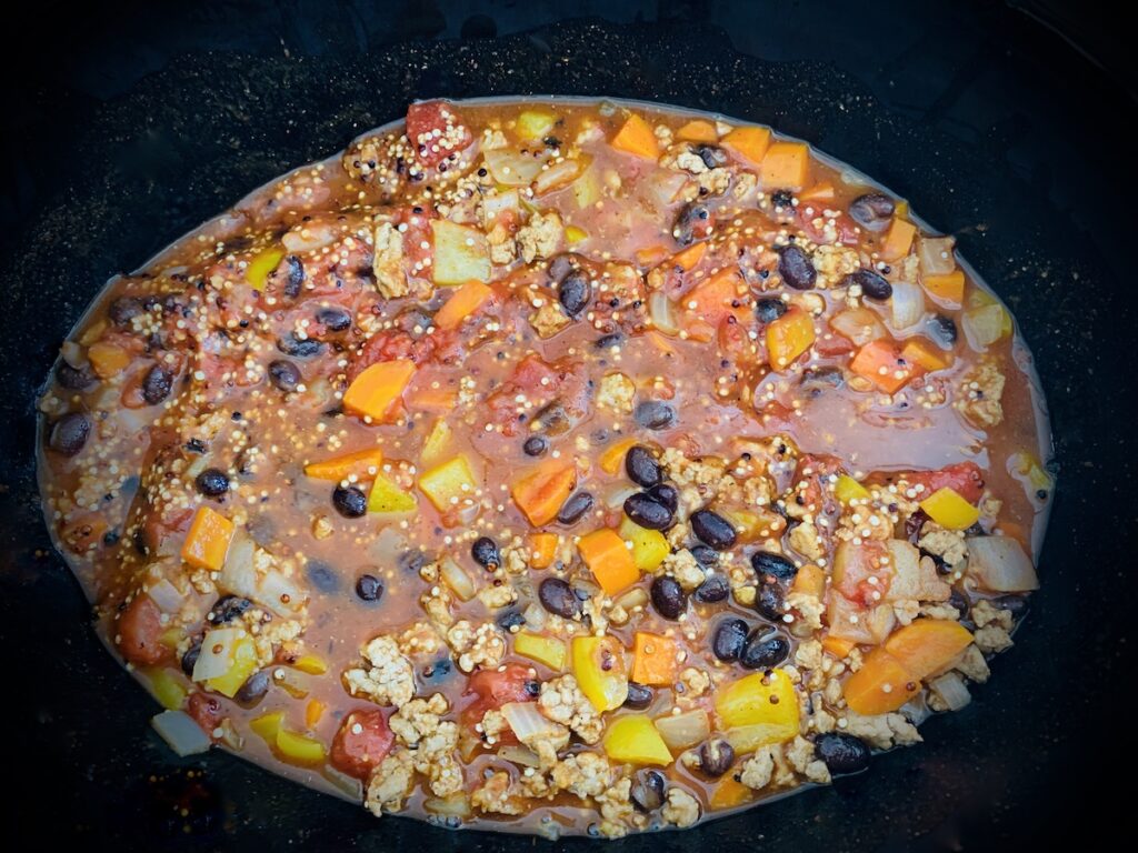 Birds eye view: uncooked chili ingredients in the bottom of an oval crockpot bowl.
