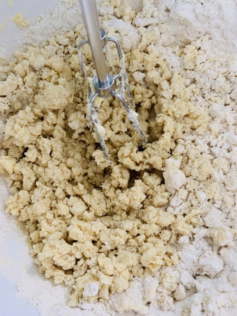 Gluten-Free dough being mixed by beaters. It is starting to look crumbly and some unmixed flour is still visible on the right side.