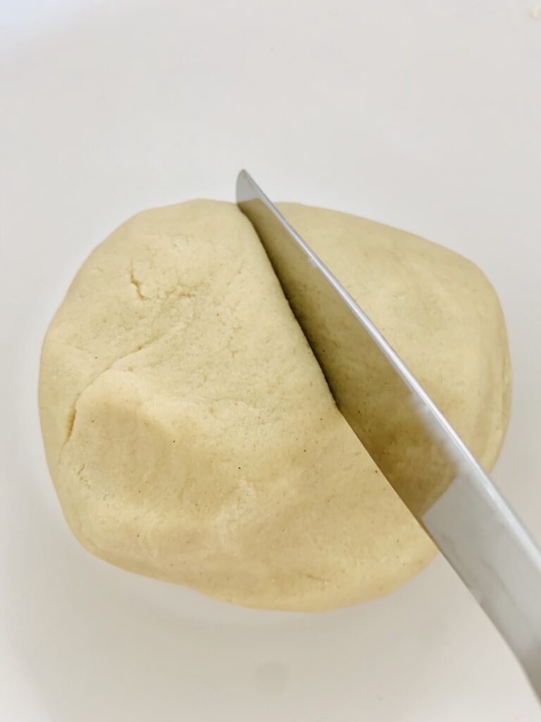 A knife cutting a ball of beige gluten-free dough in half.