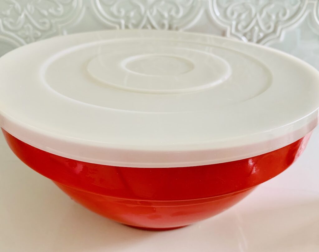A large, red bowl with a white plastic lid.