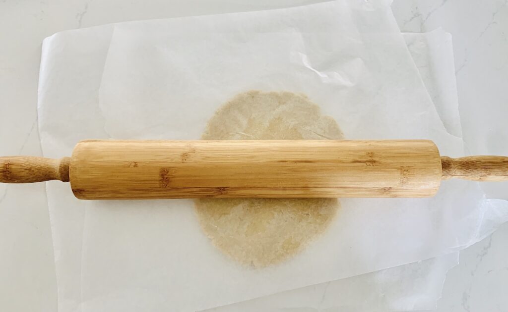 Rolling pin on top of wax paper with cookie dough underneath.