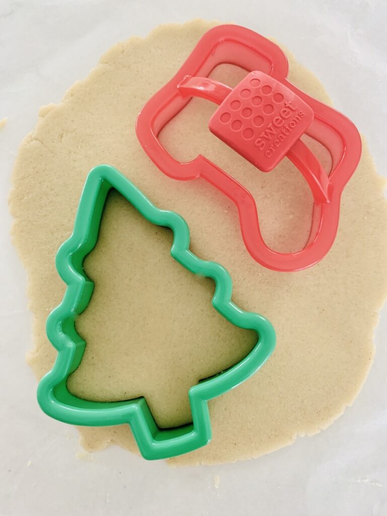 A green Christmas tree cookie cutter and red stocking cookie cutter on rolled out dough.