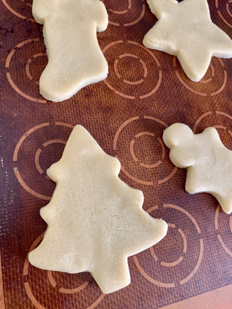 Cookie cut outs: Christmas tree, stocking, star, and holly, on a well-used silicone baking mat.