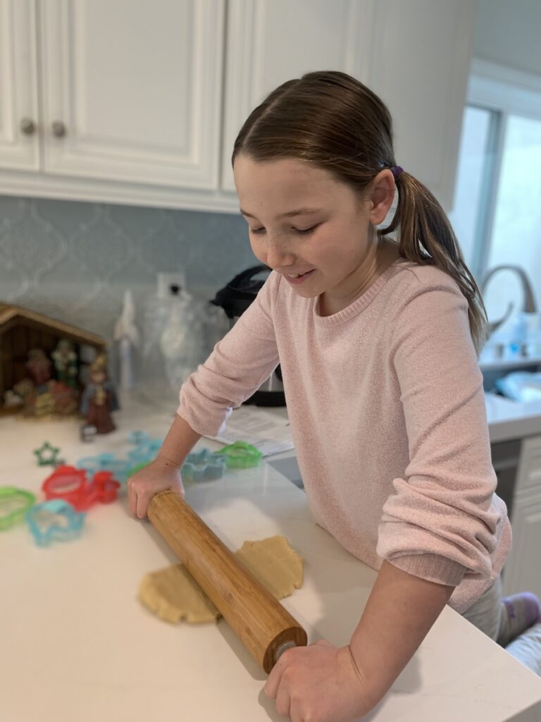Miss E with pigtails, rolling out sugar cookie dough on a white counter.