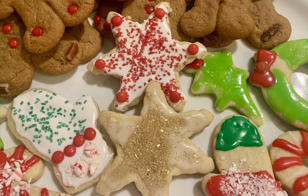 A plate of decorated gluten-free sugar cookies with part of a pile of gingerbread cookies showing in the background.