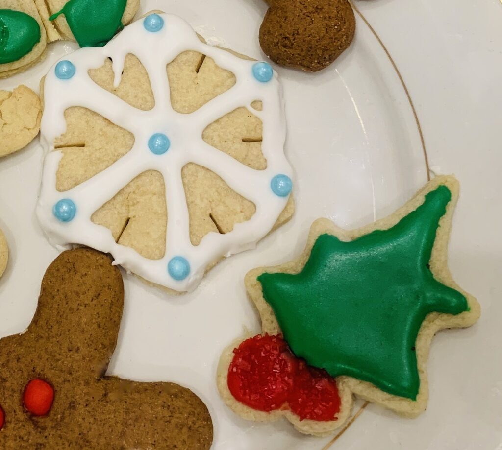 A plate with snowflake and holly gluten-free sugar cookies with parts of a couple of gingerbread cookies showing.