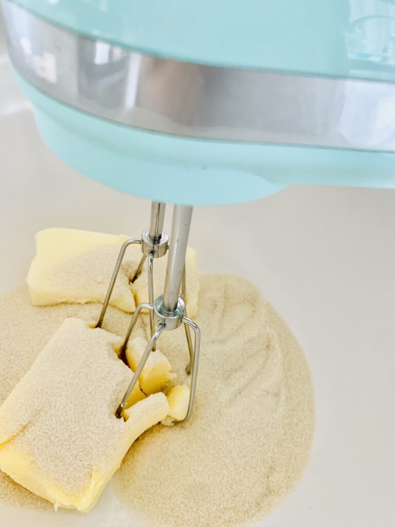 Unmixed sugar, shortening, and butter with the beaters of an aqua hand mixer sitting in the ingredients.