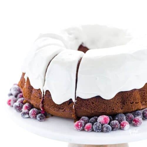 Cranberry orange bundt cake covered with white icing and surrounded sugared cranberries.