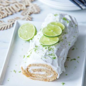 Roll of gluten free white cake topped with white frosting, lime slices and lime zest.