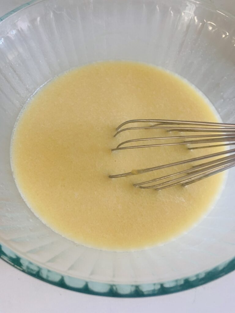 Yellow wet ingredients in a white bowl with a whisk resting in the bowl.