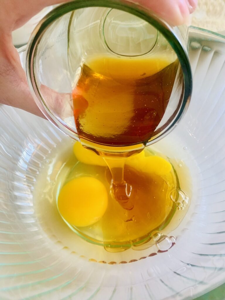 Honey being poured into a mixing bowl with 2 eggs.