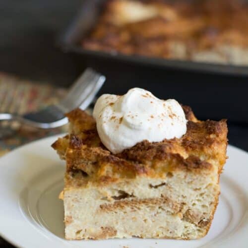 Slice of eggnog bread pudding topped with whipped cream.