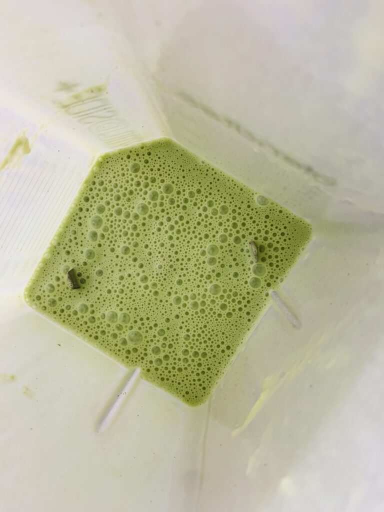 Green matcha crepe batter in the bottom of a blender, with visible bubbles from being freshly mixed.