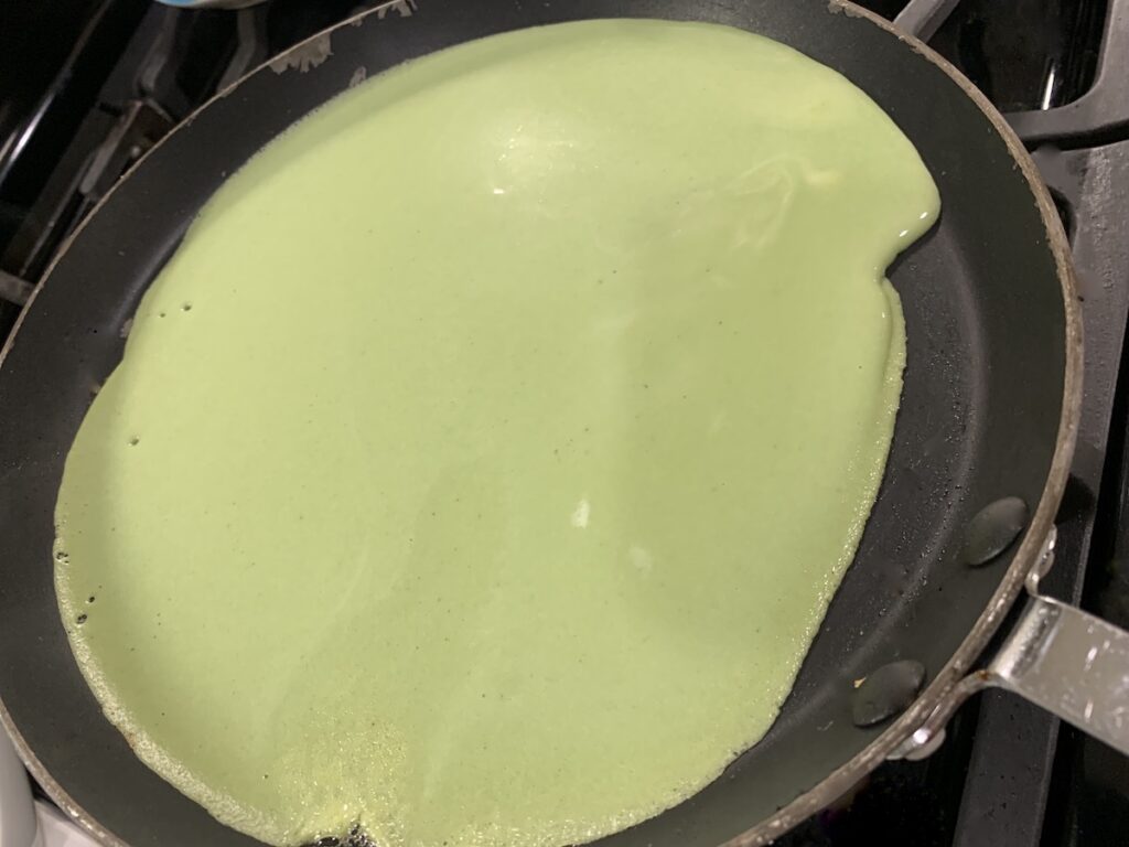 Green batter in a crepe pan with a small edge not yet fully coated with batter.