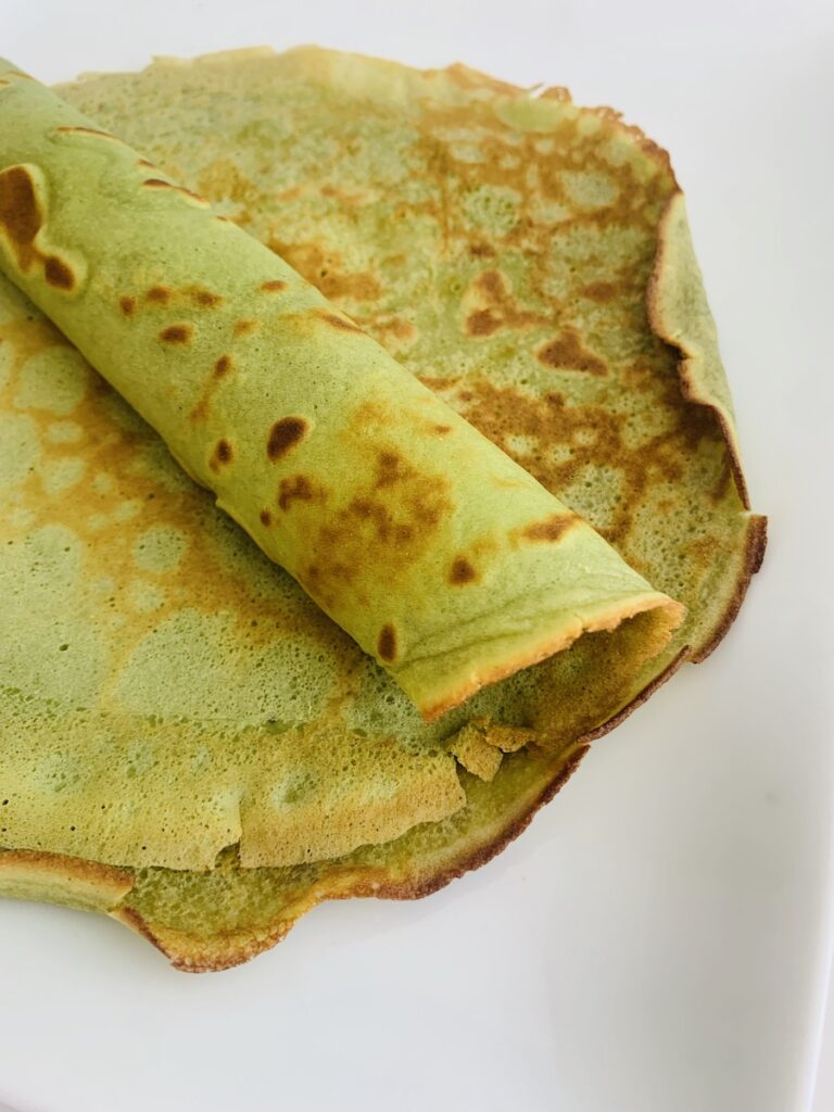 A couple of bright green crepes, with the top crepe half rolled.
