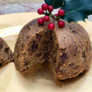 Gluten-free Christmas pudding with a slice removed and toped with red holly.