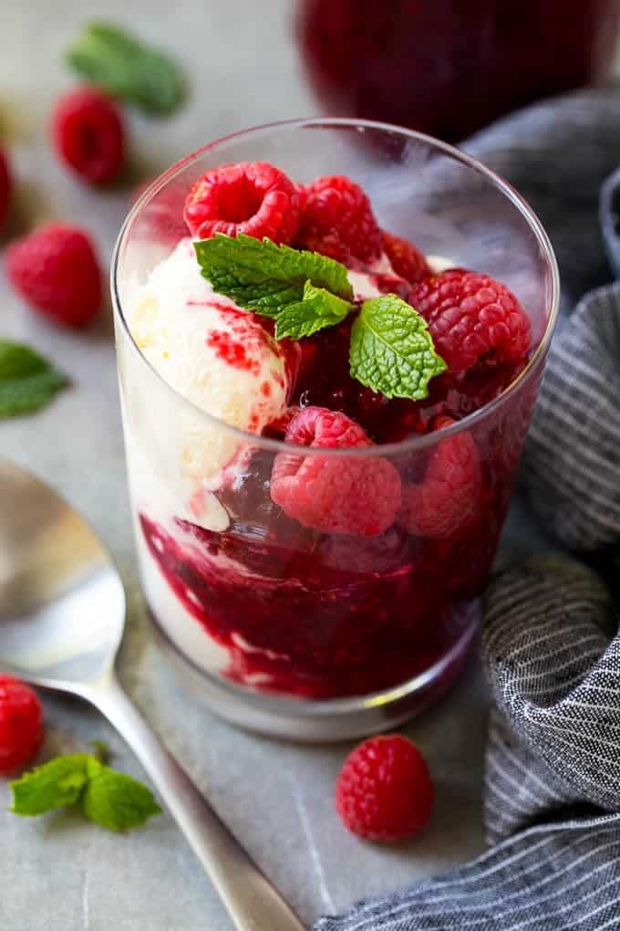 Glass of ice cream with raspberry sauce, fresh raspberries and mint.