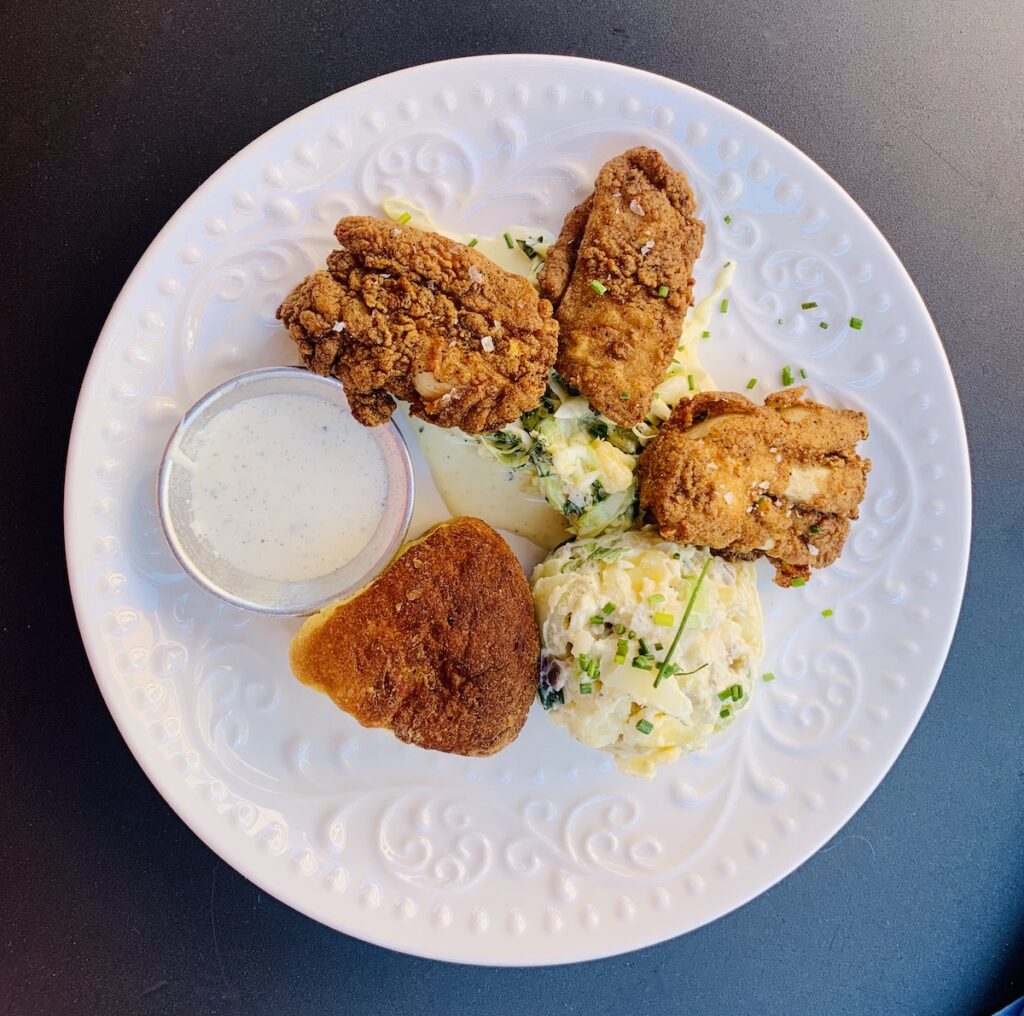 Birds eye view: plate with fried chicken, ranch, Cole slaw, scoop of potato salad and a roll.
