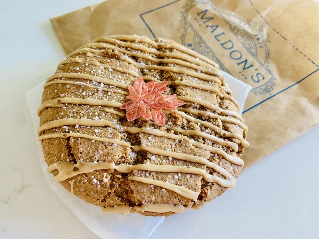 A chai cookie with light brown drizzled icing and an edible leaf on top.