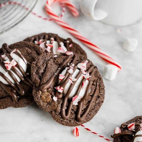 chocolate cookies with marshmallow, crushed candy canes & chocolate drizzle on top. Candy cane in the background.