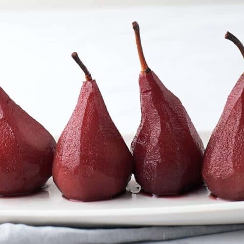 Four deep red poached pears on a white plate.