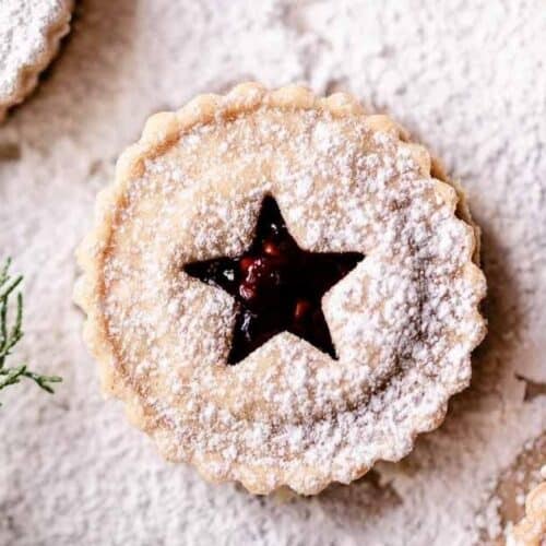 Bird's eye view: liner cookie with star cut out and red jam revealed, sprinkled with powdered sugar.