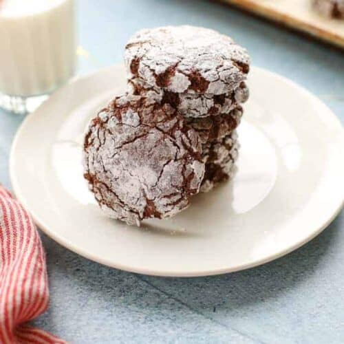 Chocolate crinkle cookies with powdered sugar coating, on a white plate.