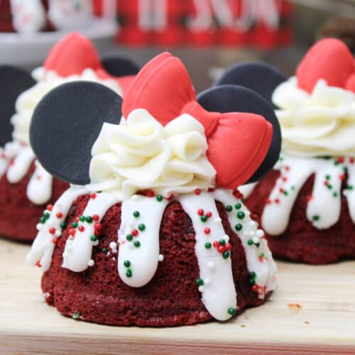 Minnie Mouse themed red velvet bundt cakes with sprinkles, whipped cream, white frosting, black ears, and a red bow.