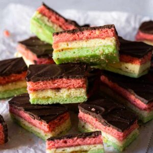 Italian rainbow cookies with layers of red/pink, white, and green sponge cake, topped with chocolate icing.