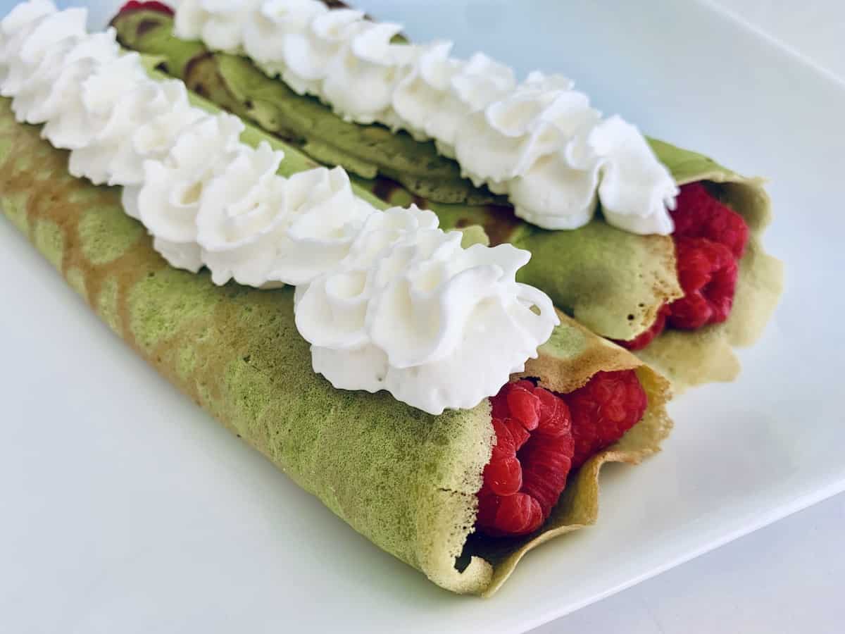 2 green crepes filled with raspberries, topped with whipped cream.