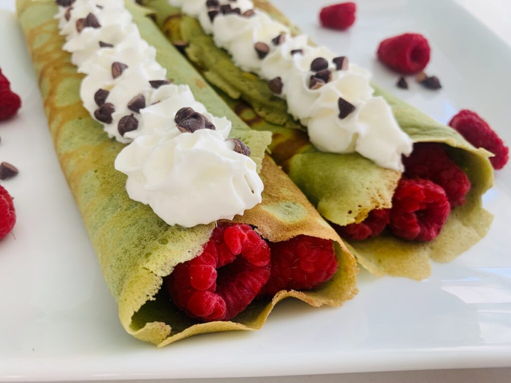 2 green crepes filled with raspberries, topped with whipped cream and mini chocolate chips.