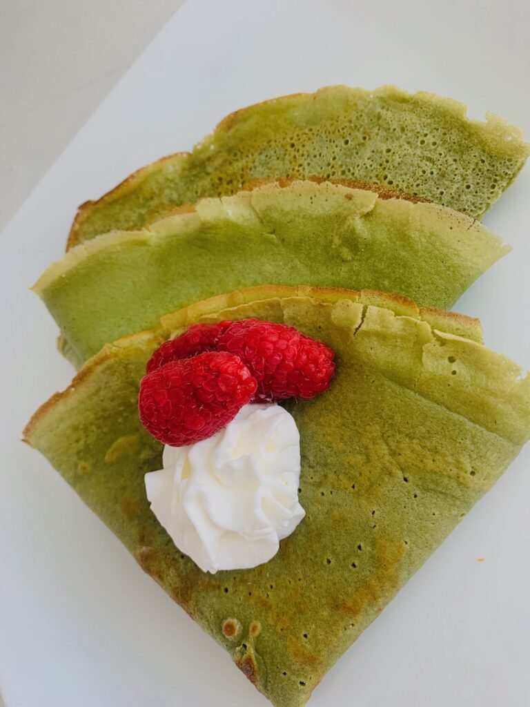 3 green crepes folded into triangles and topped with a dollop of whipped cream and a few raspberries.