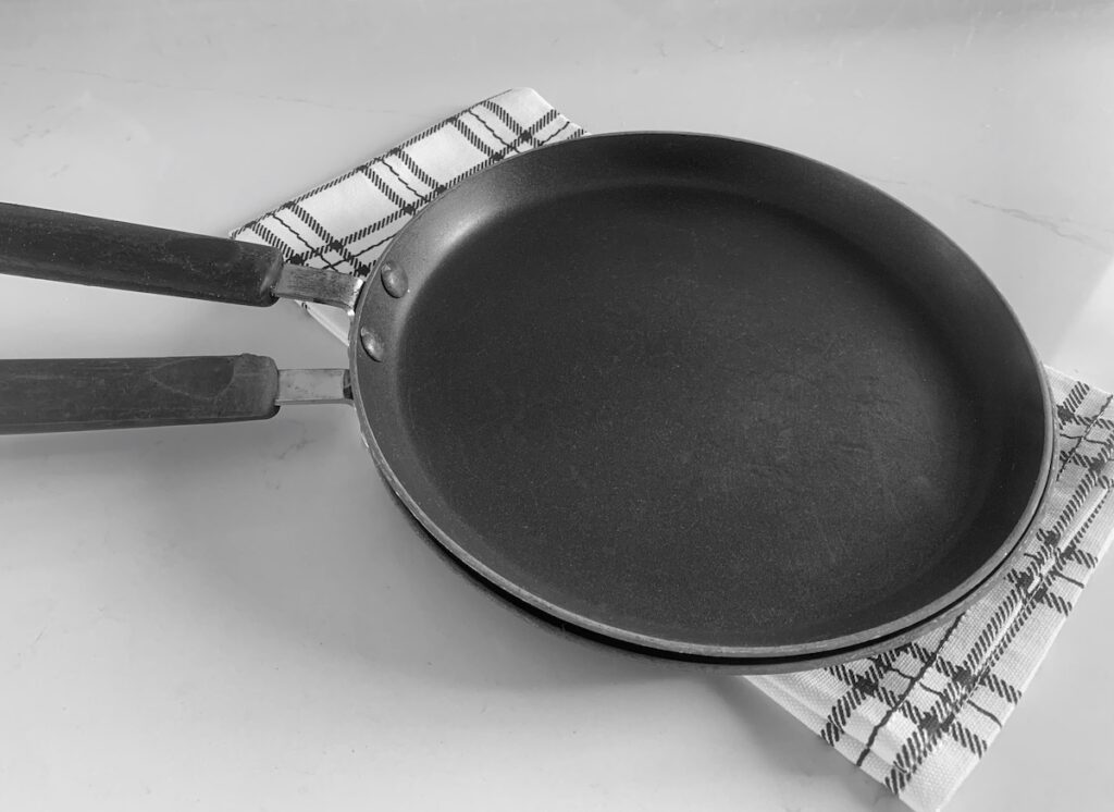 2 crepe pans stacked on top of a black and white plaid dish towel.