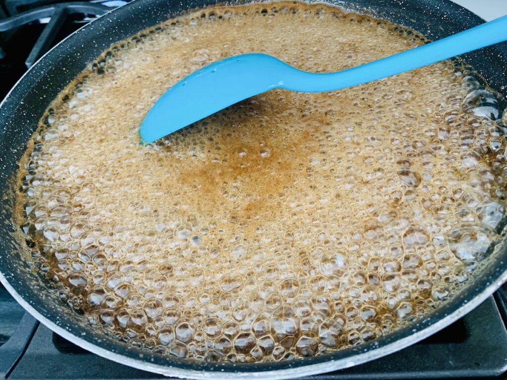 Bubbling, boiling, brown liquid in a frying pan, being stirred by an aqua spoon.