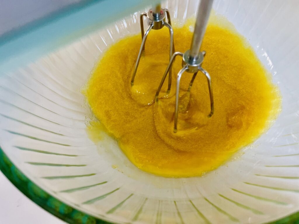 Beaters mixing dark yellow colored mixture in a glass bowl.