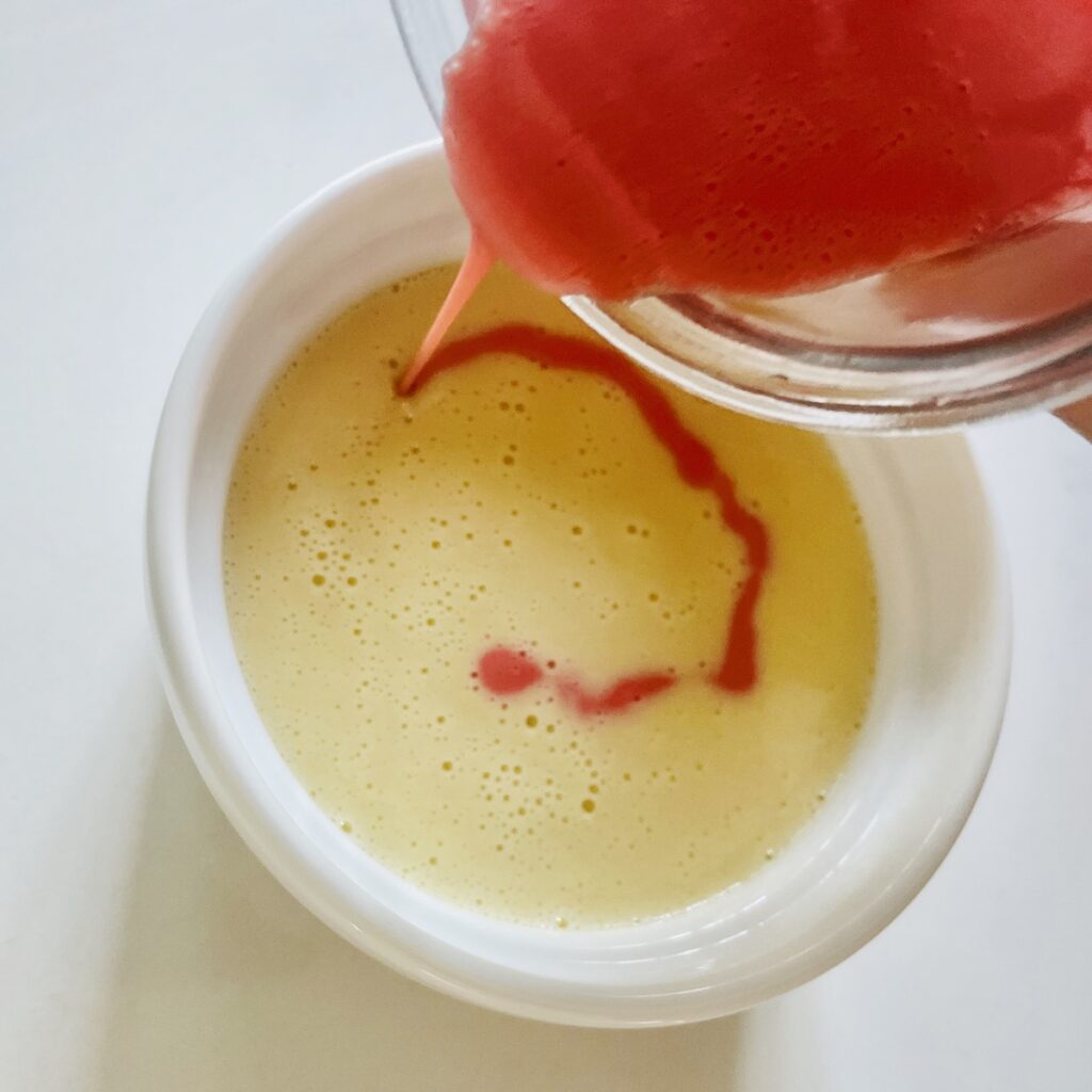 Birds eye view: red batter drizzled in a circle on top of cream-colored batter in a ramekin.