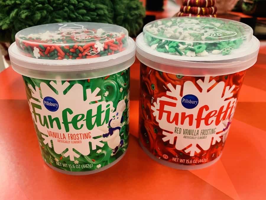 Tubs of red and green gluten-free Funfetti frosting with sprinkles in the lid.