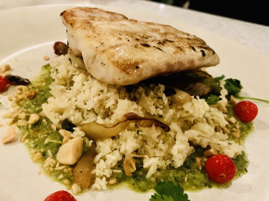 White pan-seared fish on to of a bed of rice and pesto sauce. Garnished with fresh herbs and cherry tomatoes.