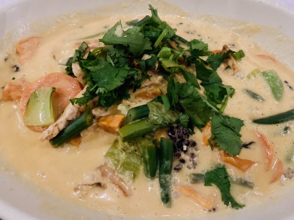 Bowl of chicken, quinoa, and vegetables in a creamy, orange, curry sauce, and topped with fresh herbs.