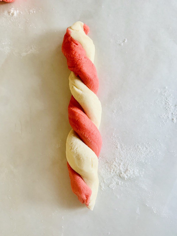 Overhead view: a red dough strip twisted with a white dough strip.