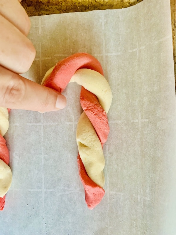 Overhead view: fingers curling down the top of the twisted red & white dough to form a candy cane hook at the top.