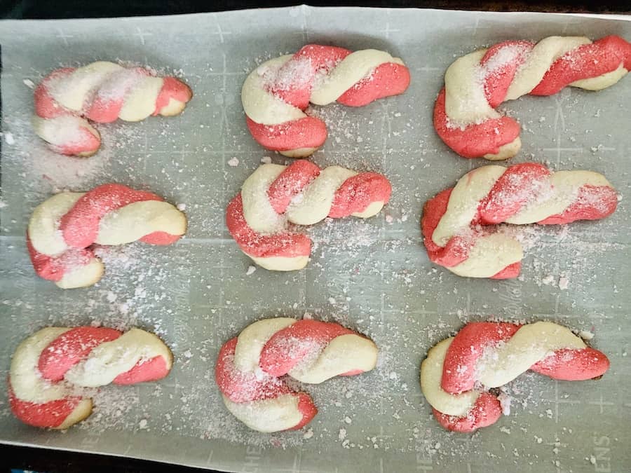 Overhead view: 9 candy cane cookies on a baking sheet, sprinkled with candy cane sugar.