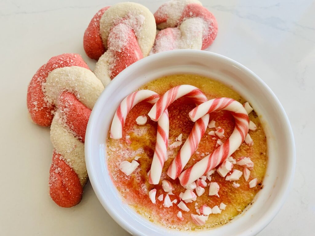 Birds eye view: 3 gluten-free candy cane cookies next to a ramekin of candy cane creme brûlée topped with crushed candy canes and 3 whole mini candy canes.