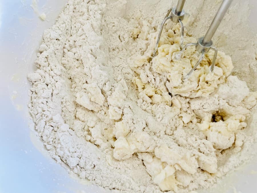 Overhead view of beaters mixing dough that is floury and crumbly.