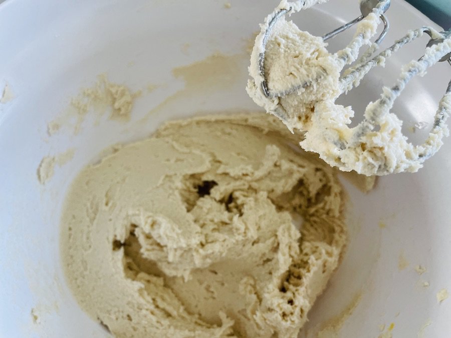 Beaters with cream-colored dough, over a bowl with smooth dough.